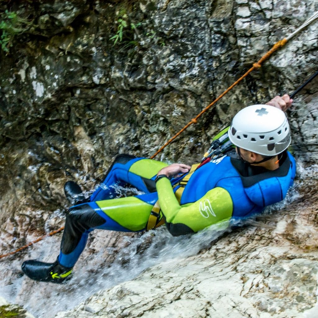 A person in neoprene suit is sliding down a small waterfall in Sušec canyon.