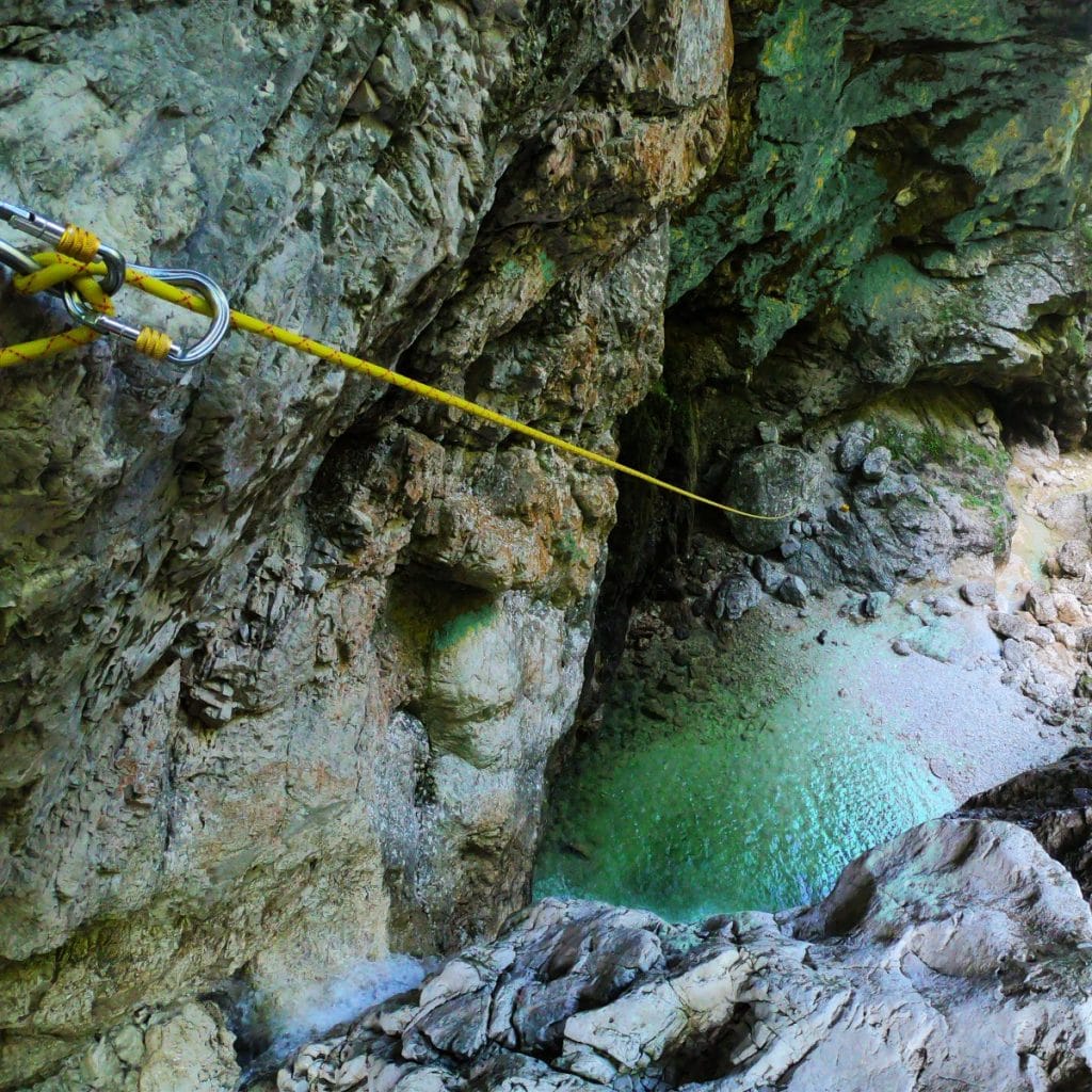 A yellow rope is attached to a rock to make a zip-line while canyoning in Bovec.